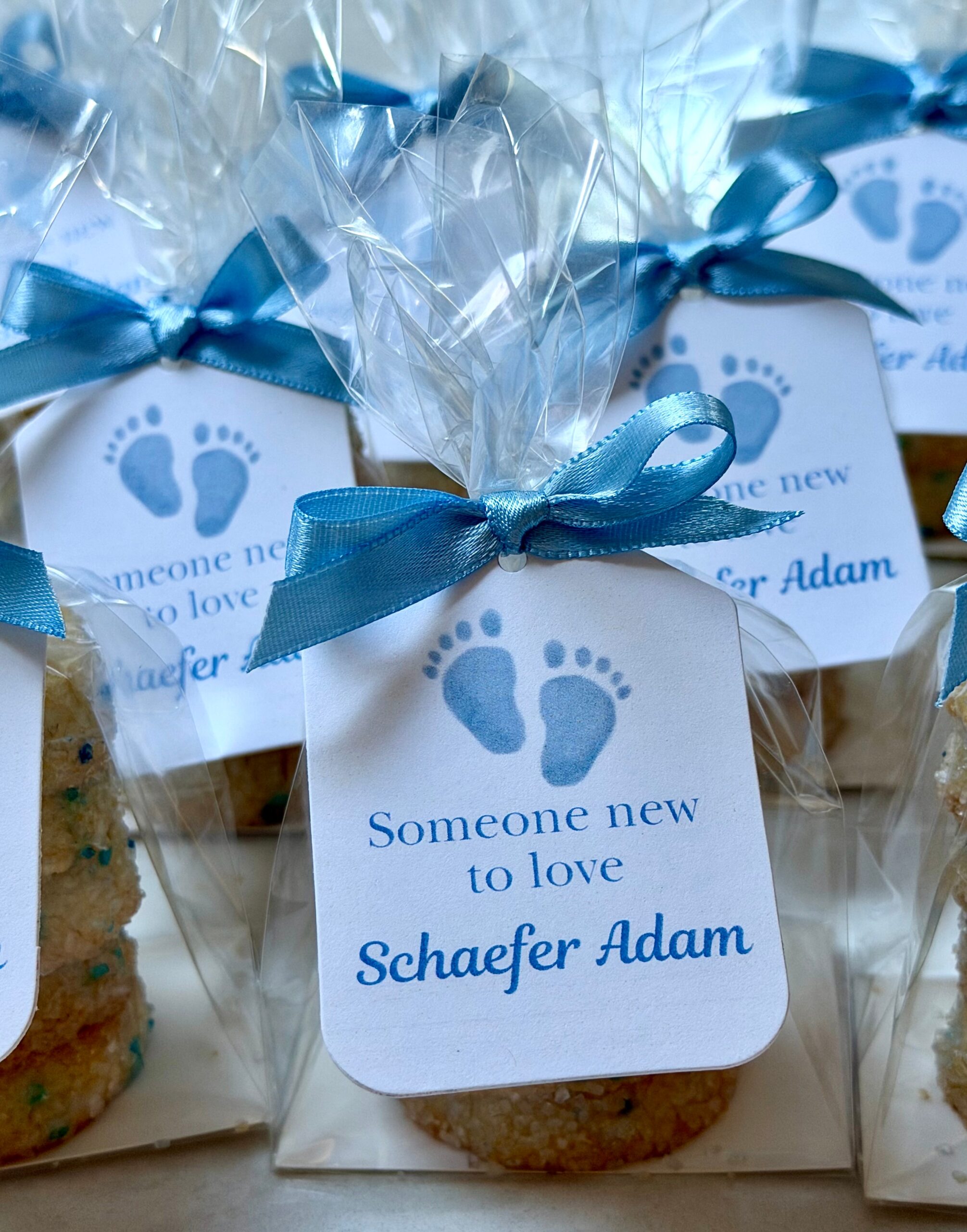 Custom baby shower cookie favors with blue footprint tags reading Someone new to love